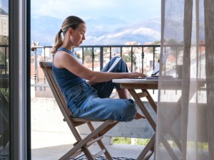 Eine Frau sitzt auf einem Balkon und arbeitet am Laptop