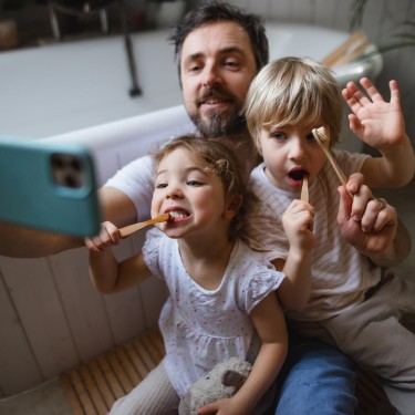 Vater putzt gemeinsam mit seinen zwei klinen Kindern die Zähne und macht ein Selfie