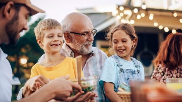 Ein Großvater hat seine beiden Enkel bei einem Gartenfest auf dem Schoß