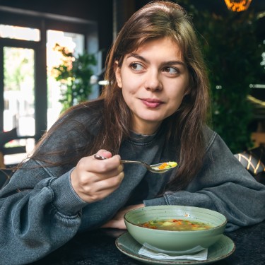 Junge Frau löffelt eine Gemüsesuppe