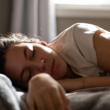 Eine Frau liegt seitlich auf einem Bett und schläft.