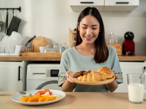 Junge Frau hat die Wahl zwischen Obst und Gebäck. Sie entscheidet sich für das Gebäck.