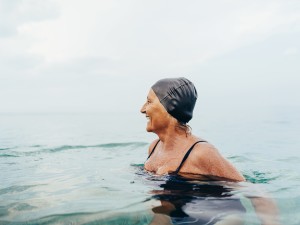 Eine ältere, agile Frau schwimmt in einem See und lächelt. 