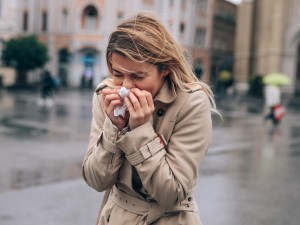 Frau läuft durch den Regen und putzt sich die Nase