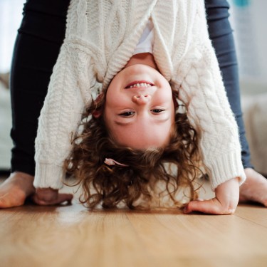 Ein Mädchen macht einen Handstand gestützt von einem Elternteil